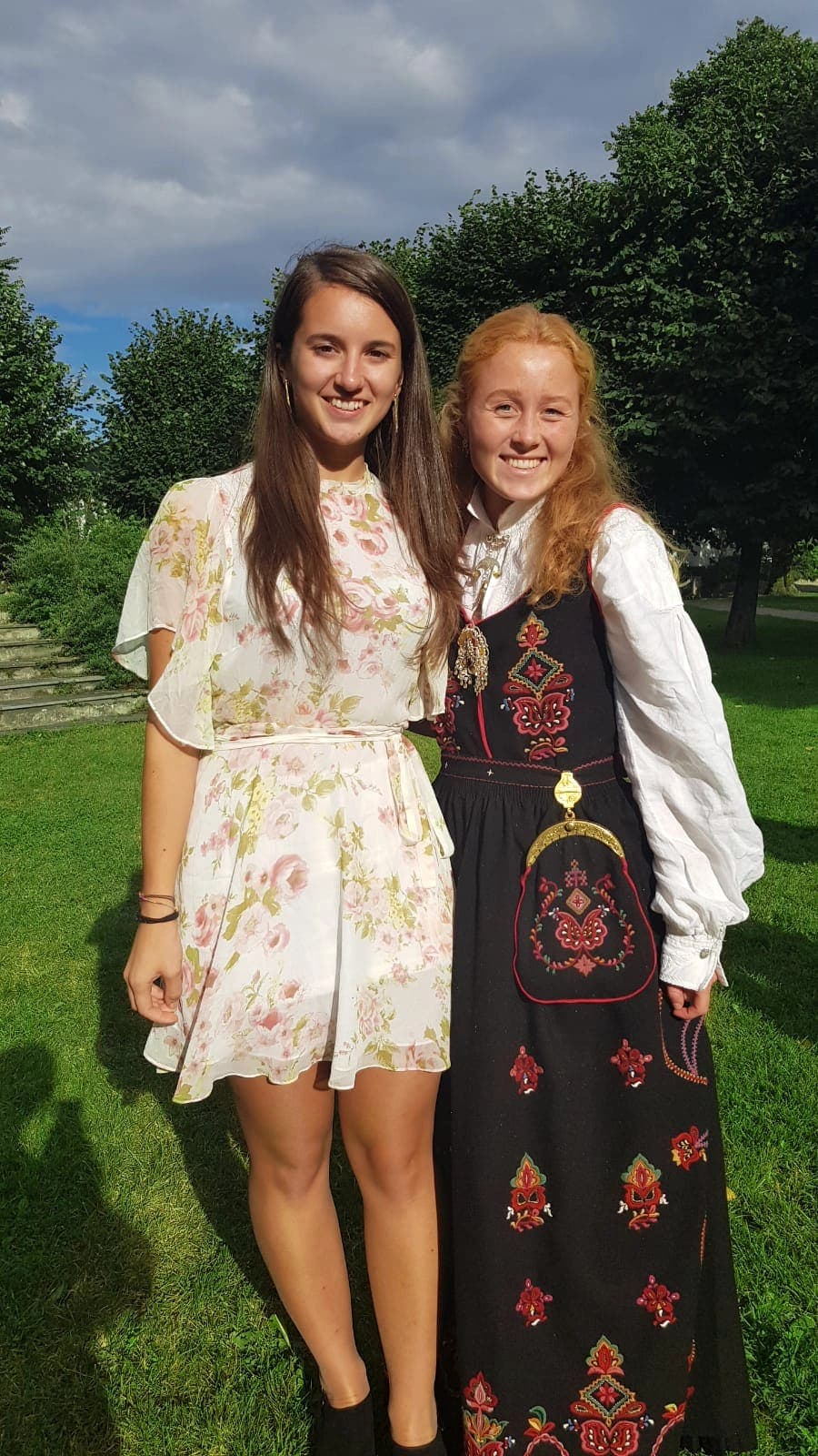Zwei Mädchen lächeln zusammen, eines trägt traditionell norwegische Kleidung, eine unvergessliche Erfahrung von Freundschaft und kulturellem Austausch in Norwegen während des Austauschjahres.