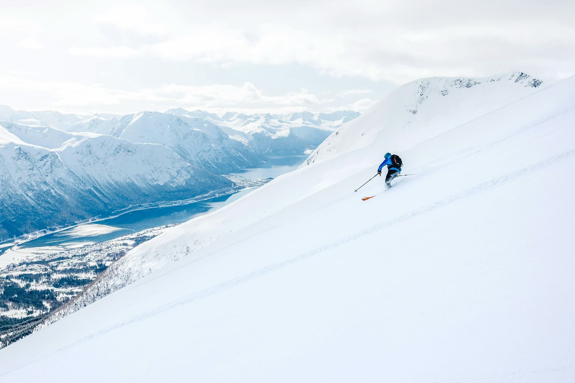 Ein Junge fährt auf Skiern einen verschneiten Hang in Norwegen hinunter, mit einem atemberaubenden Blick auf die Berge und einen Fjord, eine unvergessliche Erfahrung während des Austauschjahres in Norwegen.